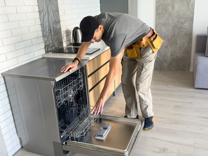 Young Repairman Service Worker Repairing Dishwasher Appliance In Kitchen